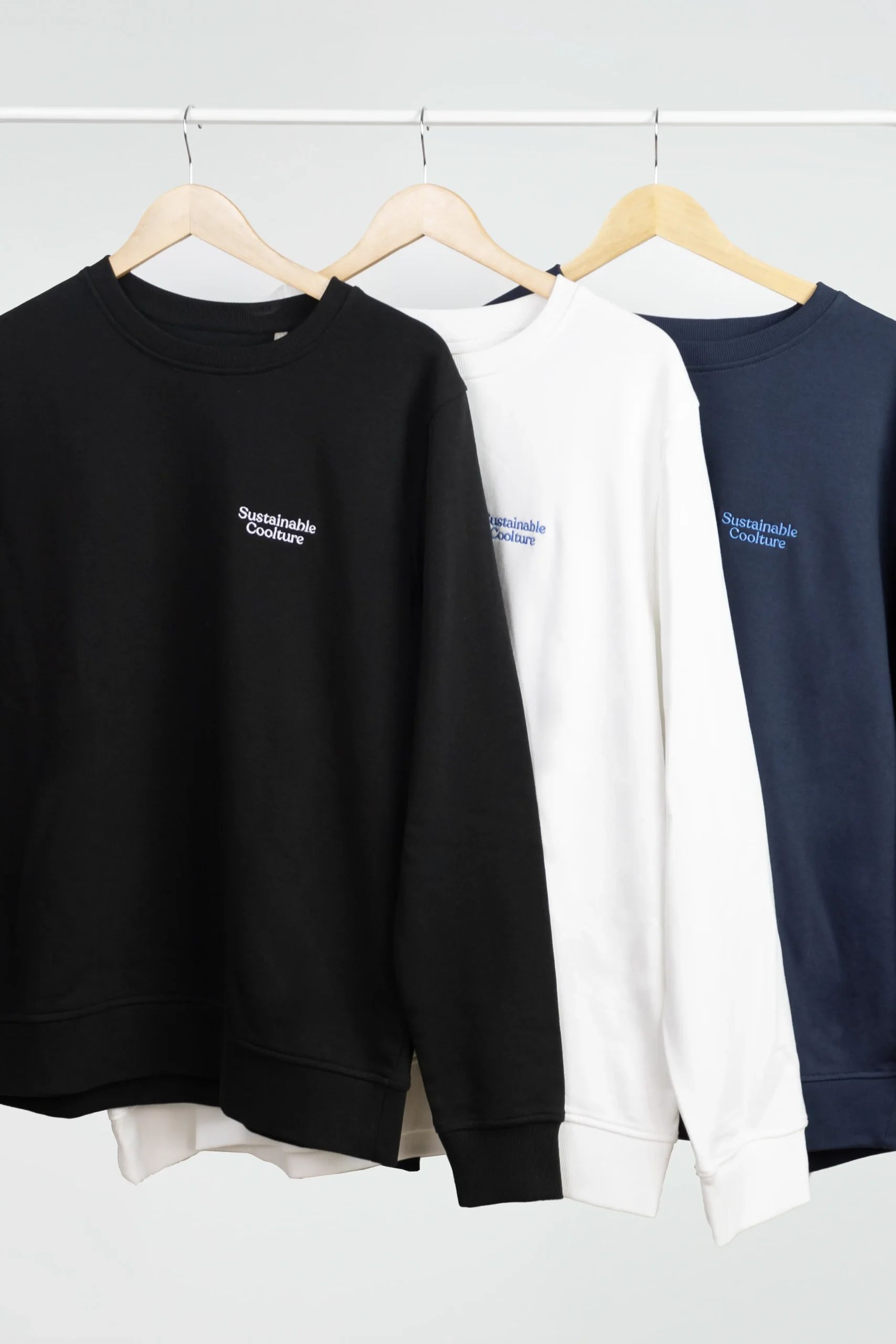 Sweats sans capuche SEDRA Tres sudaderas personalizadas de diferentes colores colgadas en perchas en un burro de ropa blanco
