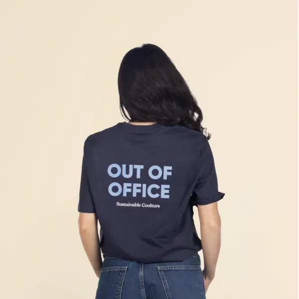 Chica morena de espaldas llevando jeans y una camiseta azul personalizada con el texto 'out of office'