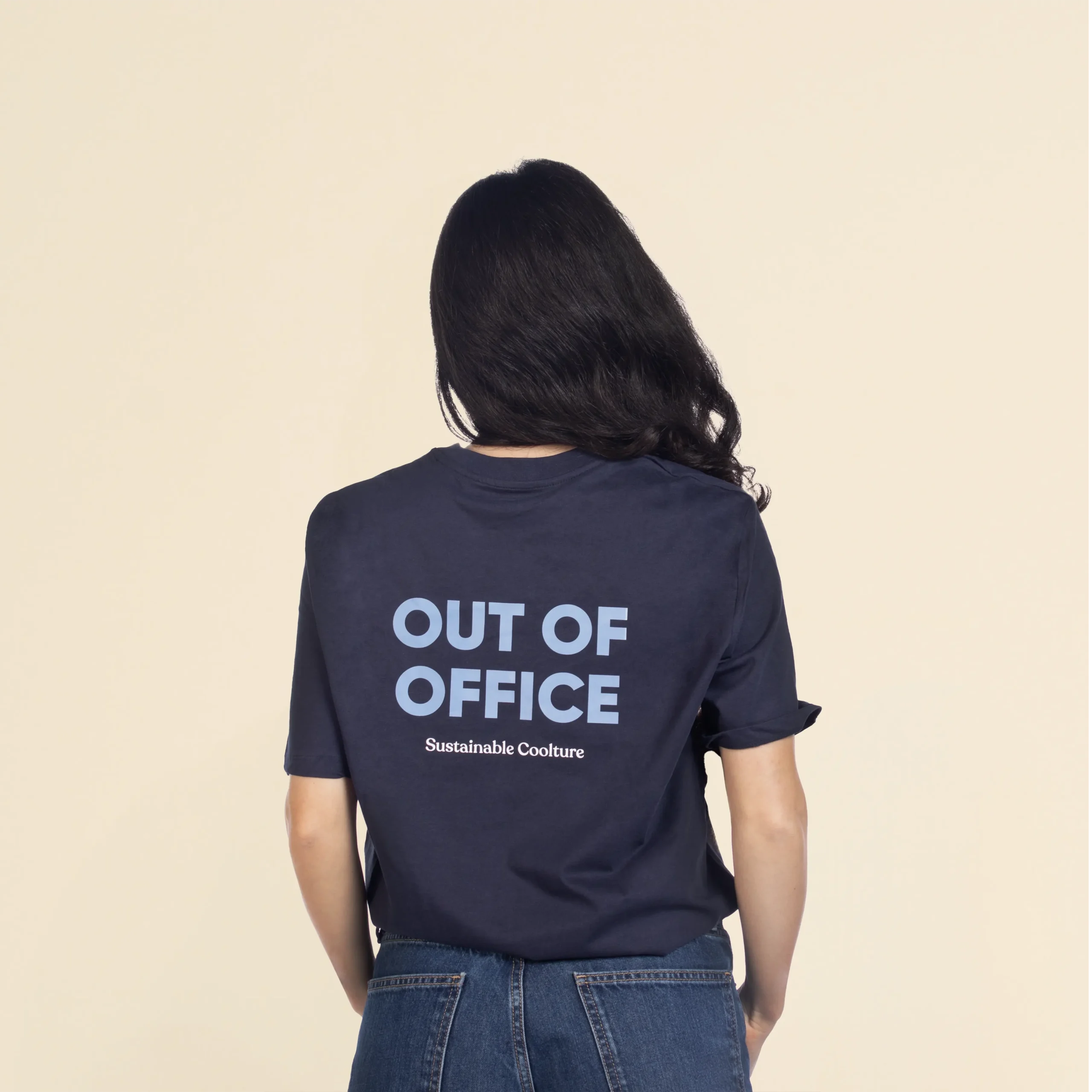 Camiseta de algodón TESSA Azul Chica morena de espaldas llevando jeans y una camiseta azul personalizada con el texto 'out of office'