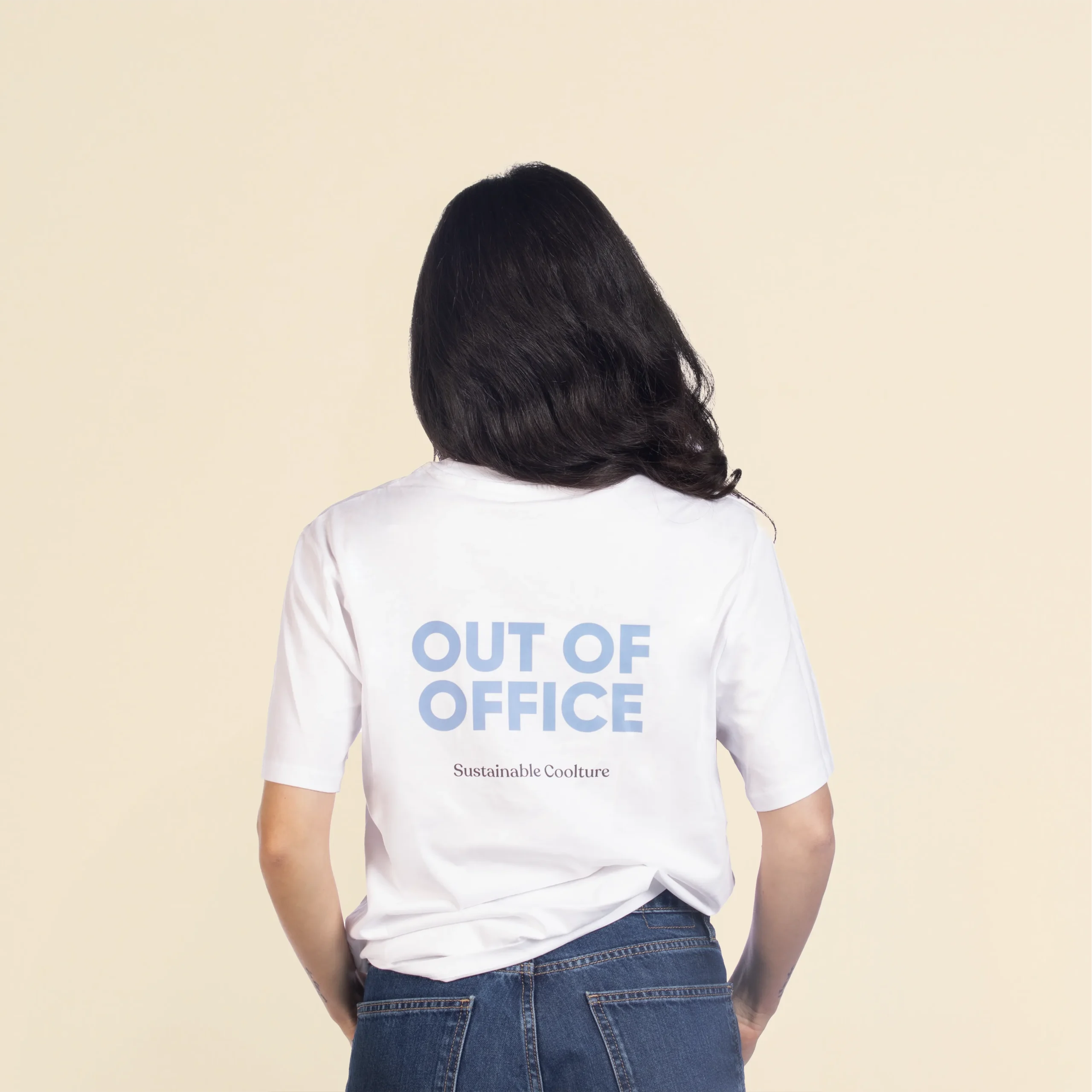 Camiseta de algodón TESSA Blanco Chica morena de espaldas llevando jeans y una camiseta blanca personalizada con el texto 'out of office'