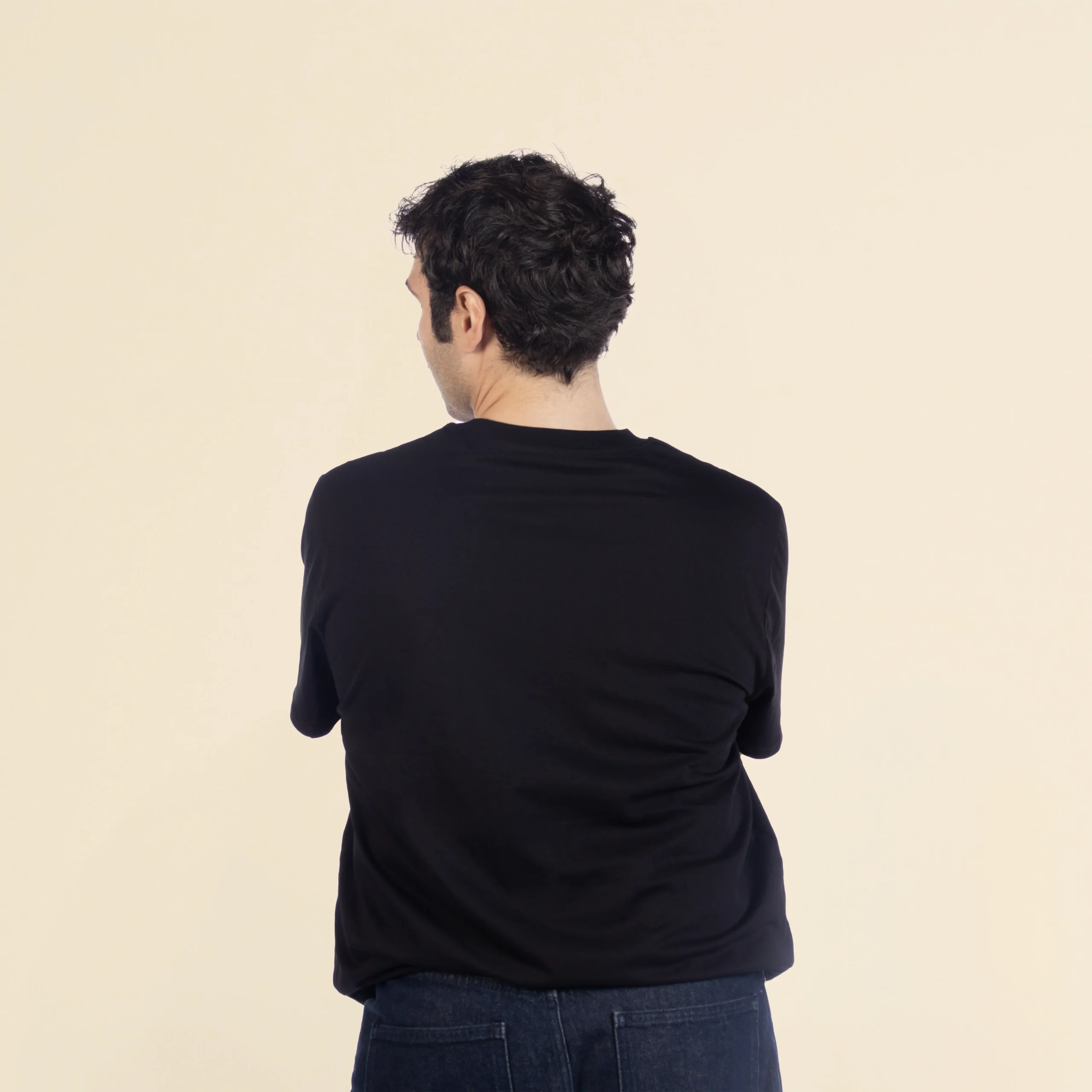 Camiseta de algodón TESSA Negro Chico moreno de espaldas llevando jeans y una camiseta de algodón negra