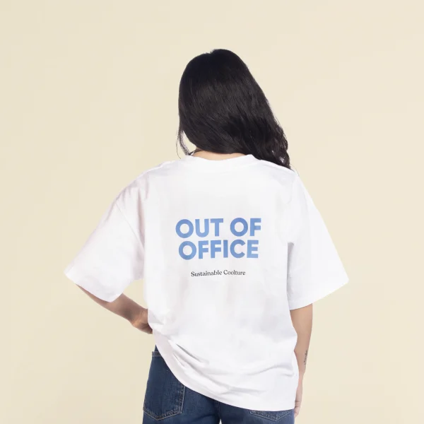 Chica morena de espaldas llevando jeans y una camiseta oversize blanca personalizada con el texto 'out of office'