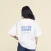 Chica morena de espaldas llevando jeans y una camiseta oversize blanca personalizada con el texto 'out of office'
