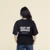 Chica morena de espaldas llevando jeans y una camiseta oversize negra personalizada con el texto 'out of office'