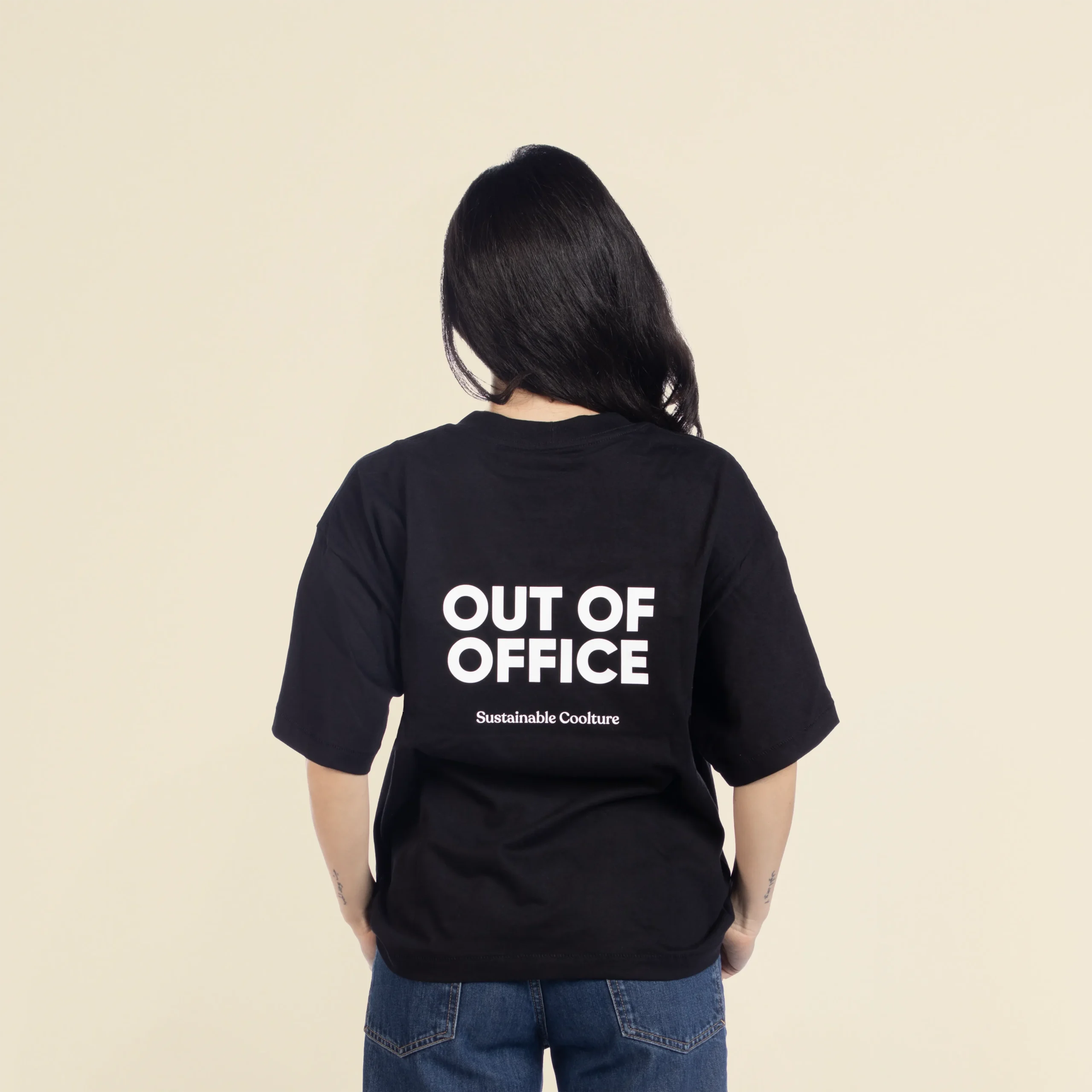 Camiseta oversize VEGA Negra Chica morena de espaldas llevando jeans y una camiseta oversize negra personalizada con el texto 'out of office'