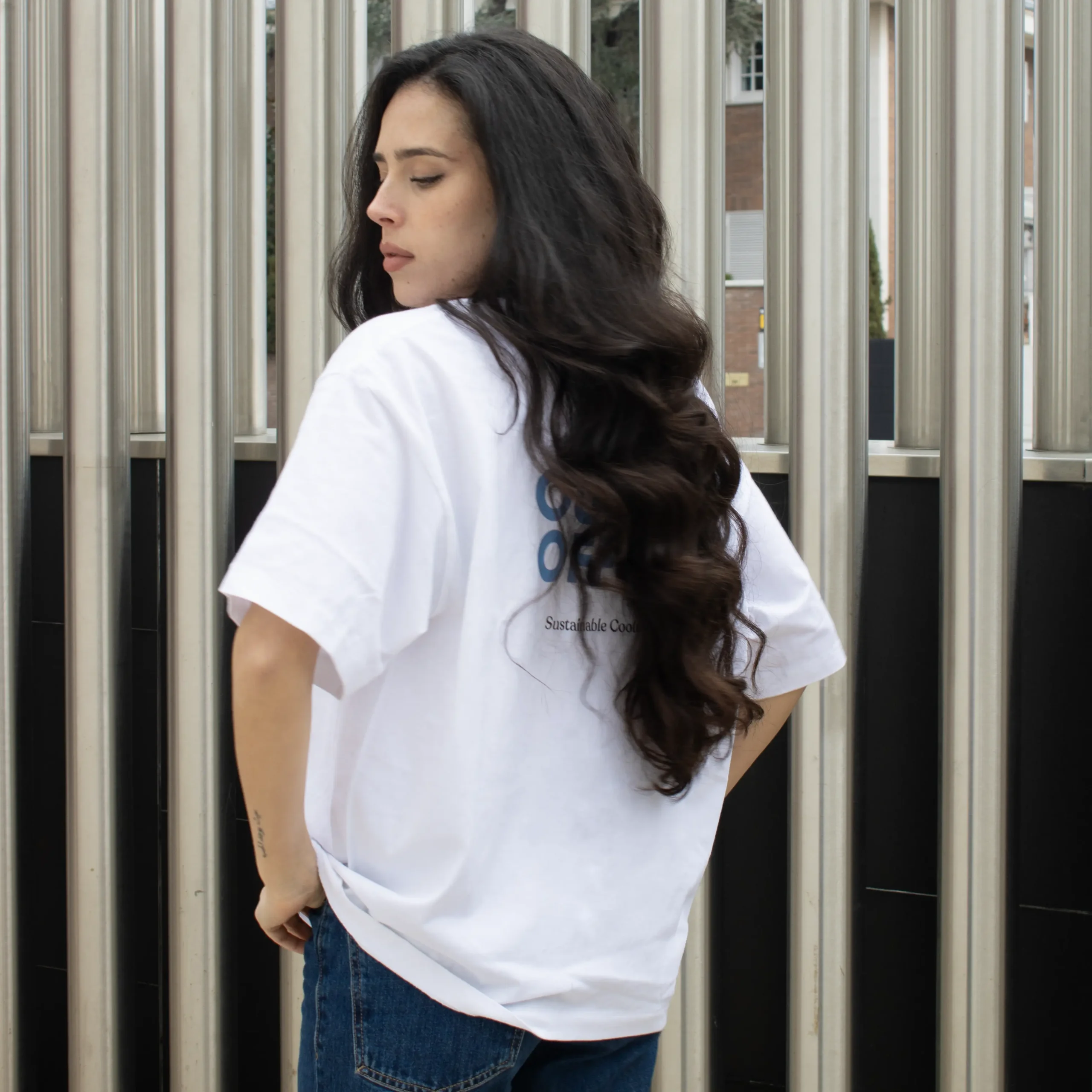 Camiseta oversize VEGA Blanca Chica morena de espaldas llevando jeans y una camiseta oversize blanca personalizada