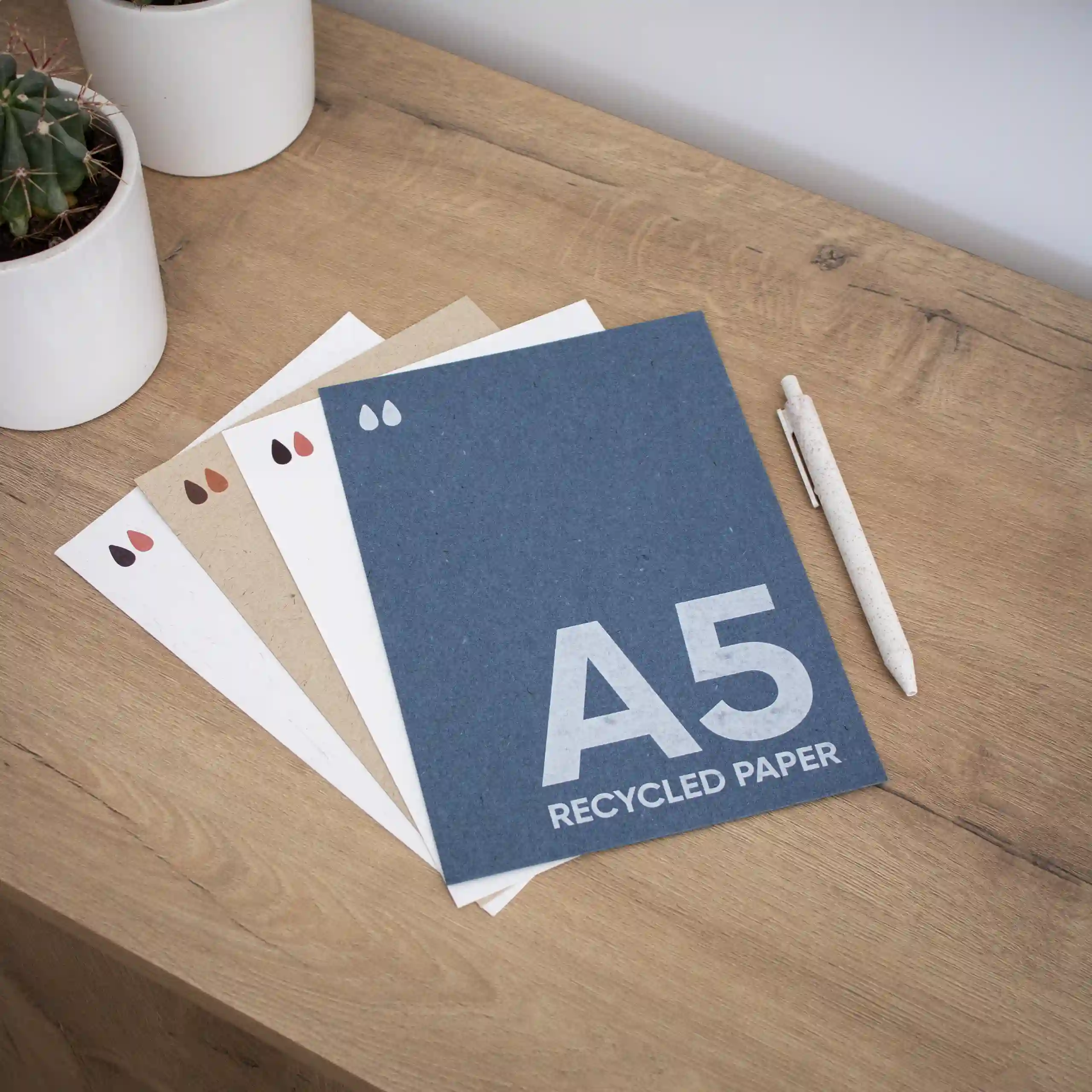 Tarjeta papel ecológico A5 Cuatro tarjetas A5 ecológicas junto a un bolígrafo sobre una superficie de madera