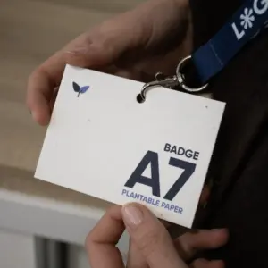 Manos sujetando una acreditación A7 impresa en papel plantable colgada de un lanyard