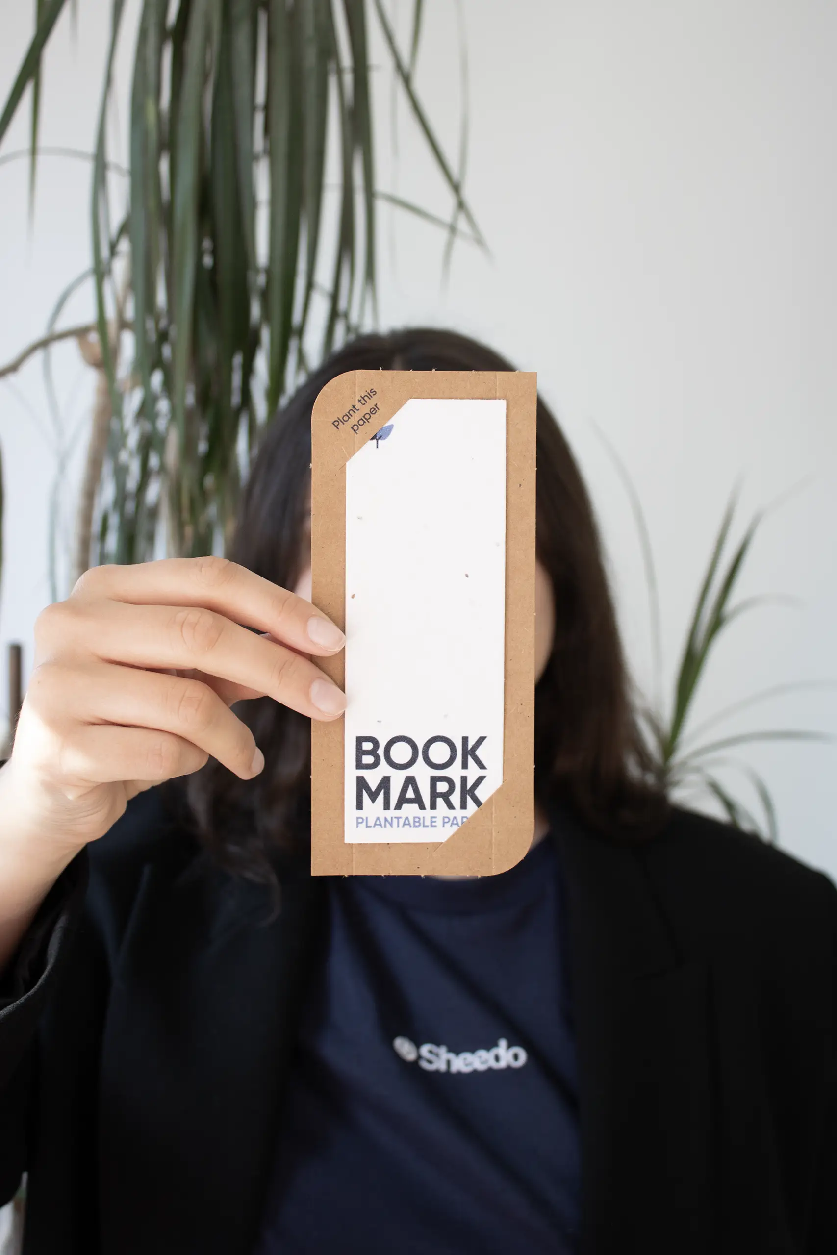 Carte kraft pour marque-pages Chica mostrando a cámara un marcapáginas impreso en papel plantable dentro de una funda en cartón kraft