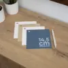 Cuatro tarjetas cuadradas impresas en papel ecológico junto a un bolígrafo sobre una superficie de madera