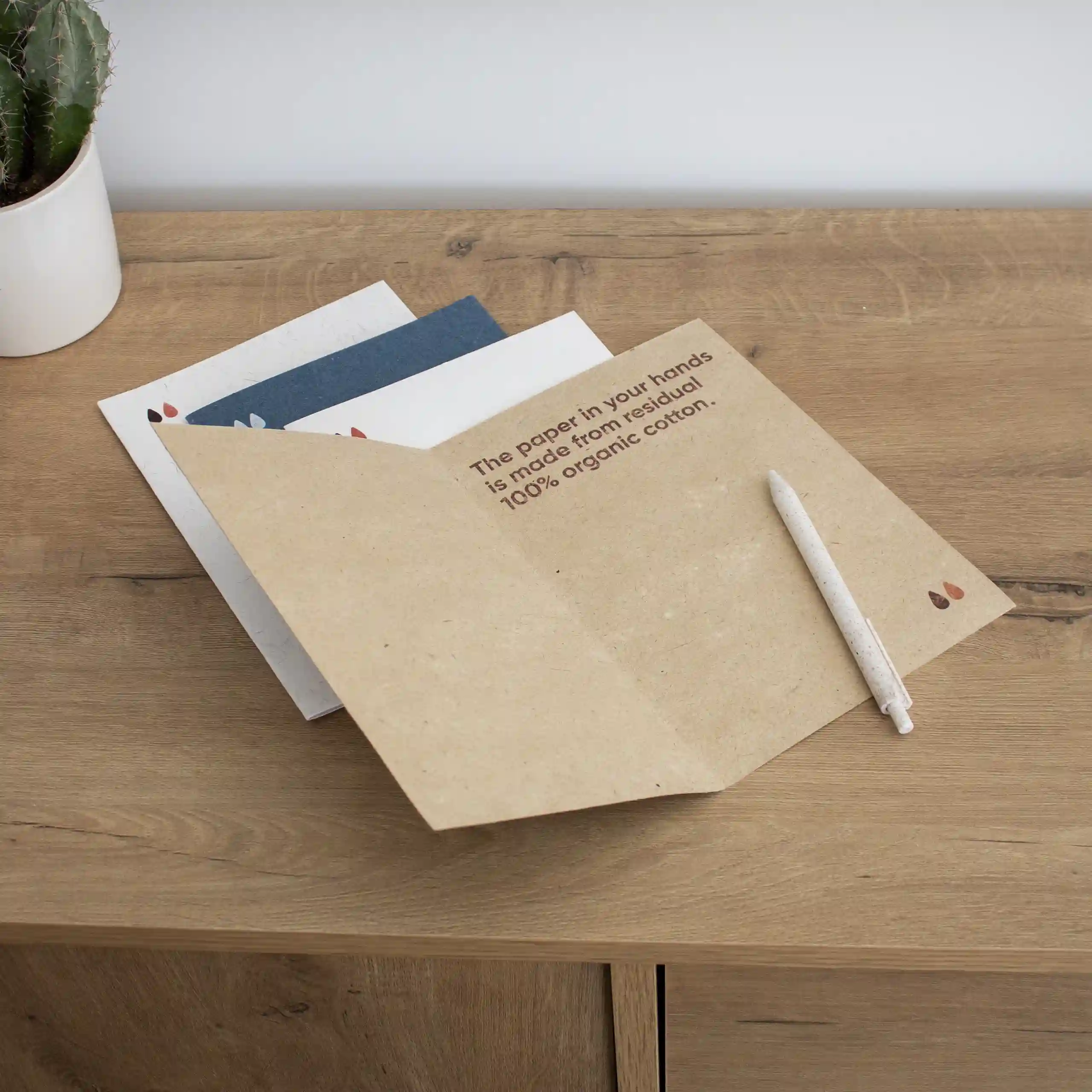 Díptico A5 de papel ecológico Cuatro dípticos A5 impresos en papel ecológico junto con un bolígrafo sobre una superficie de madera