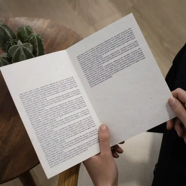 Manos sujetando un díptico A5 abierto impreso en papel plantable