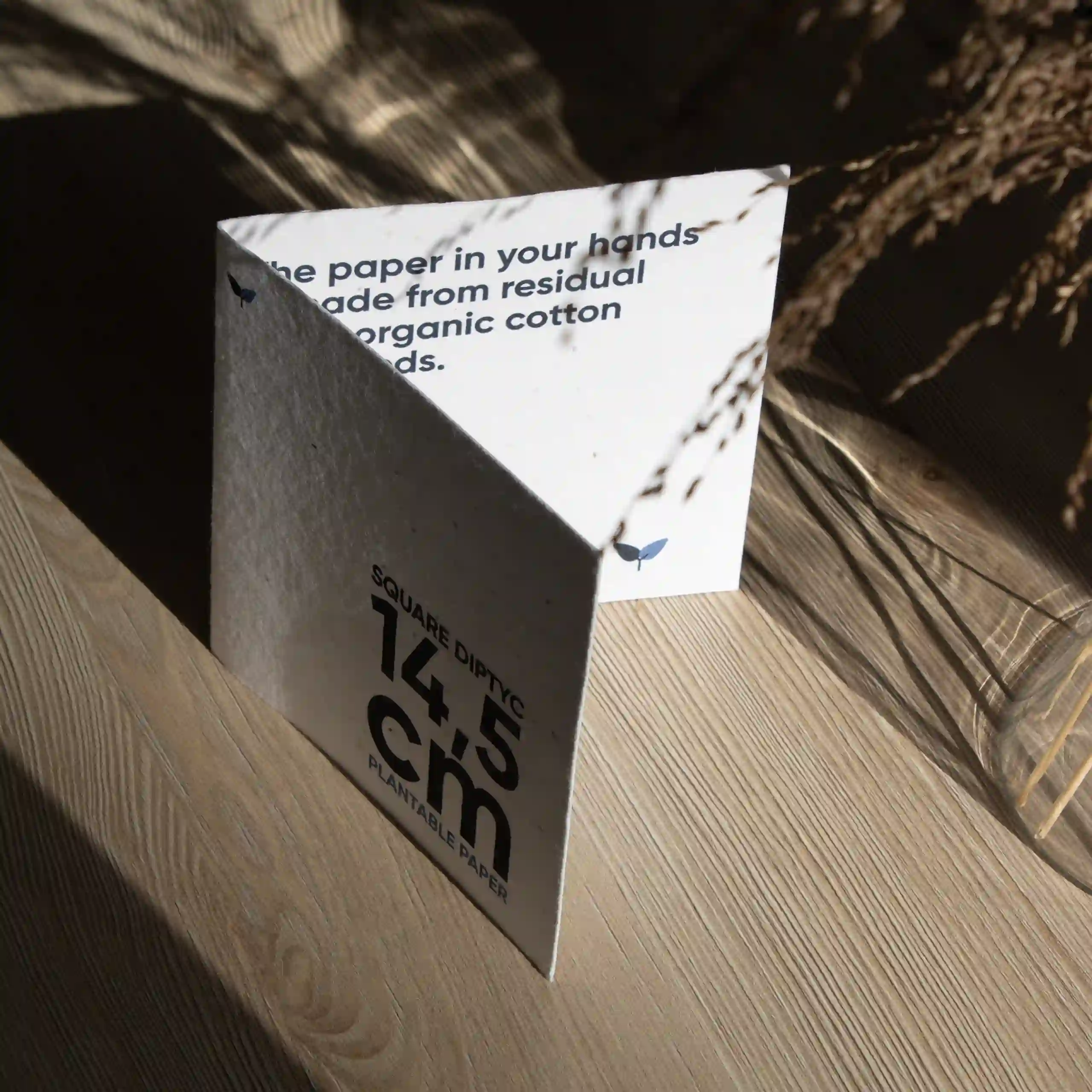 Carte pliante carrée Díptico cuadrado abierto impreso en papel plantable sobre una superficie de madera con sombras