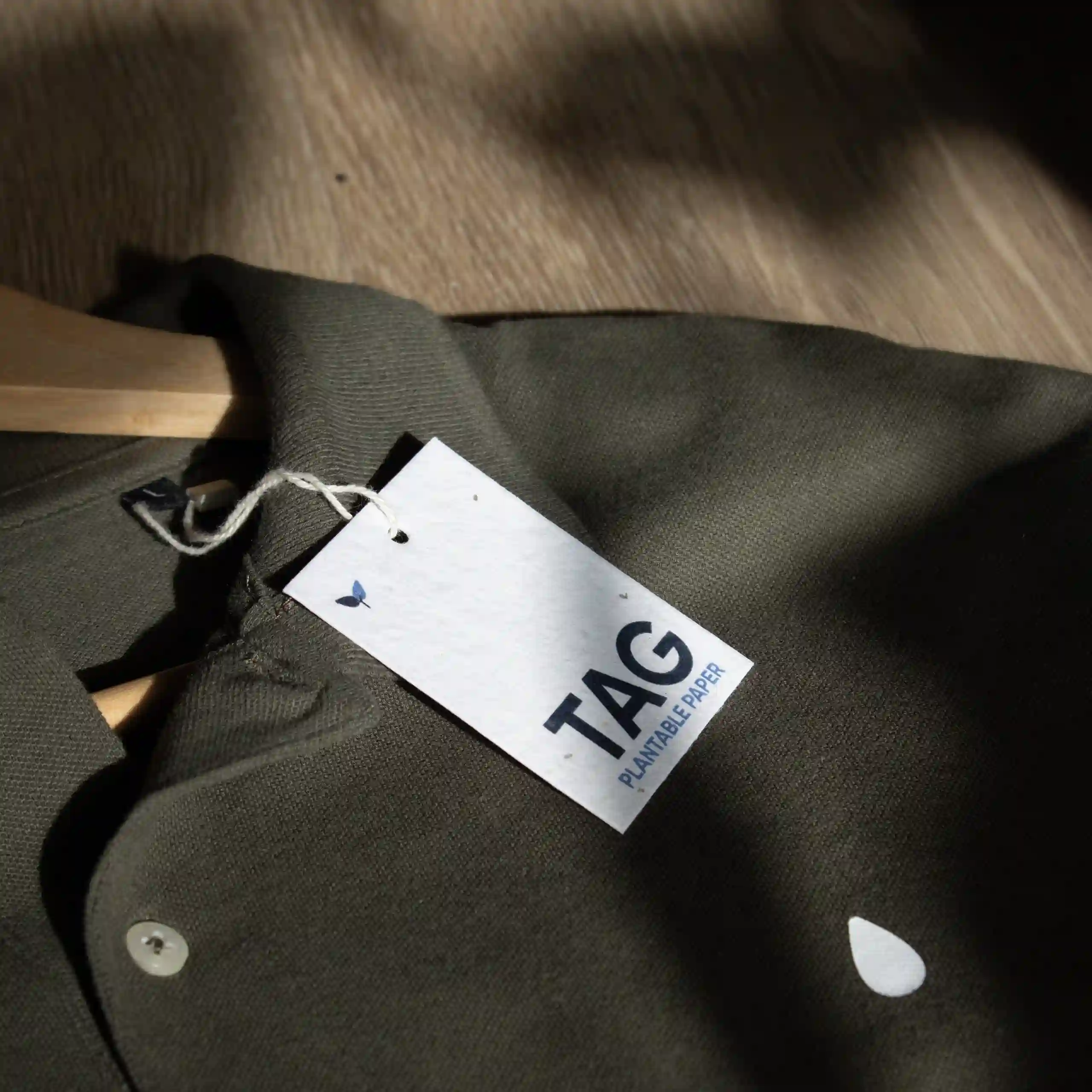 Seed paper tags Una etiqueta de ropa impresa en papel plantable colgada de un polo verde colocado sobre una superficie de madera