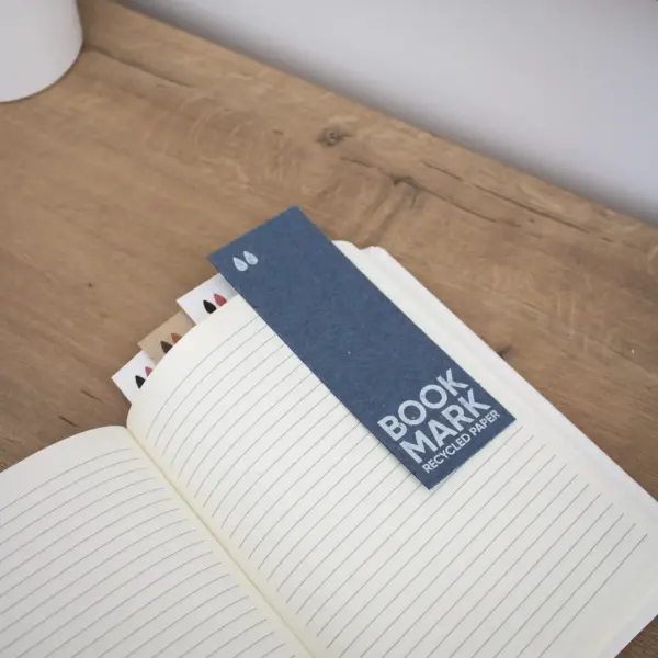 Cuatro marcapáginas de papel ecológico en un cuaderno sobre una superficie de madera
