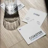 Tres posavasos de papel plantable personalizados y un vaso de cristal sobre una superficie de madera al sol