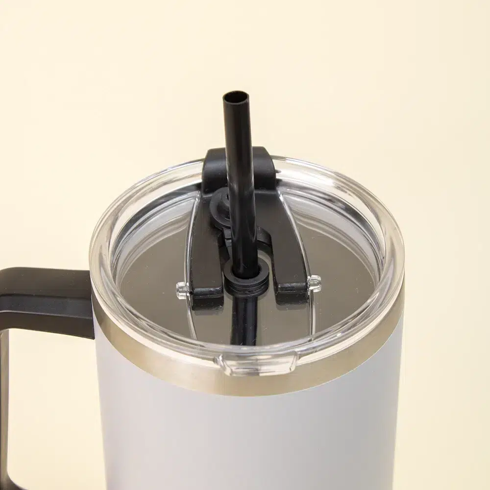 Travel tumbler EVEREST Primer plano de vaso térmico gris de acero inoxidable con pajita sobre un fondo beige