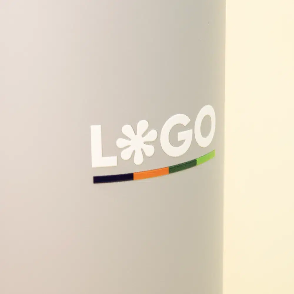 Travel tumbler EVEREST Primer plano de vaso térmico gris de acero inoxidable con logo sobre un fondo beige