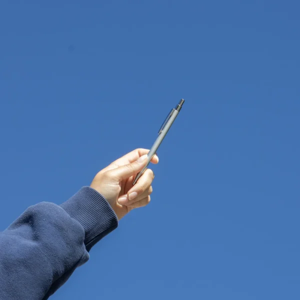 Mano alzando un bolígrafo plateado de aluminio reciclado con el cielo de fondo