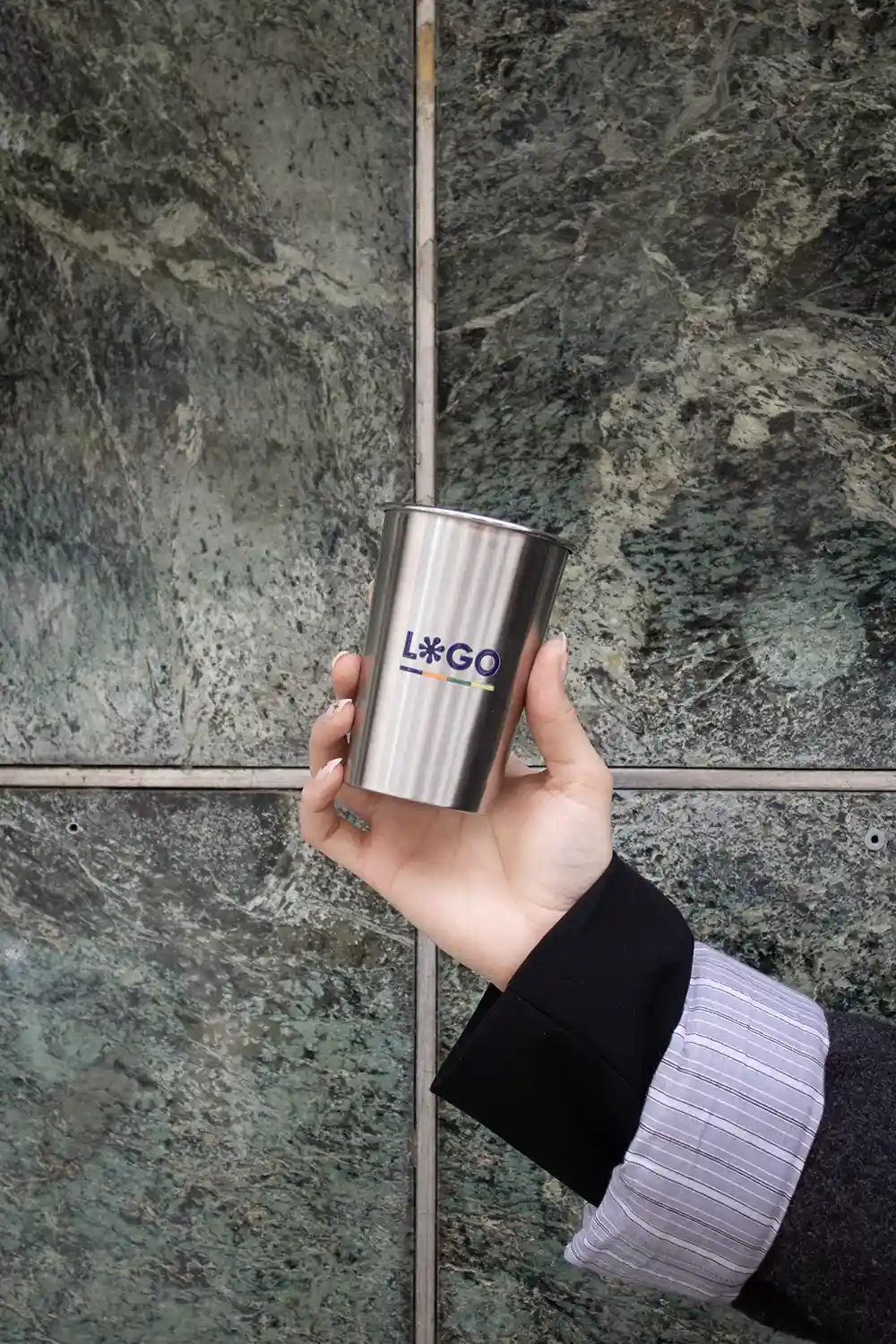 Mano sujetando vaso de acero inoxidable personalizado sobre un fondo de piedra