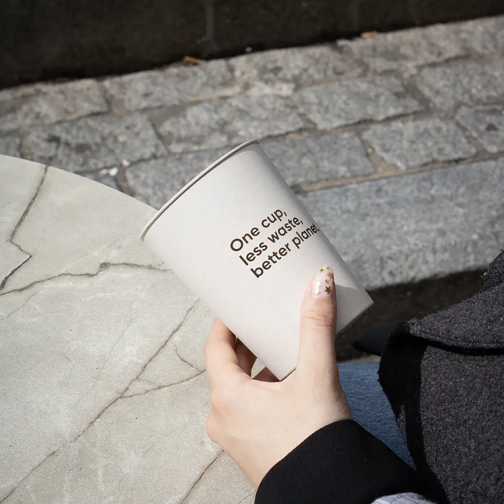 Mano sujetando vaso reutilizable de cáscara de arroz sobre un fondo de piedra