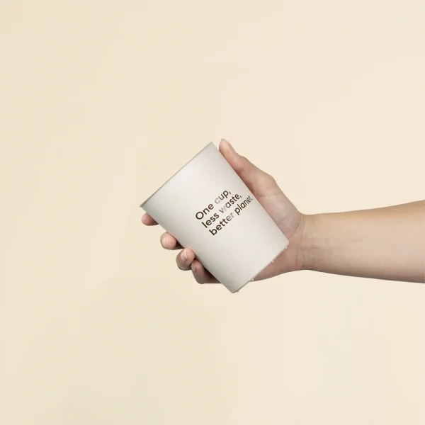 Mano sujetando vaso reutilizable de cáscara de arroz sobre un fondo beige