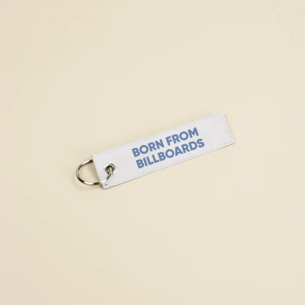 Llavero hecho con lona reciclada blanca personalizado con el texto impreso en azul: "Born from billboards"