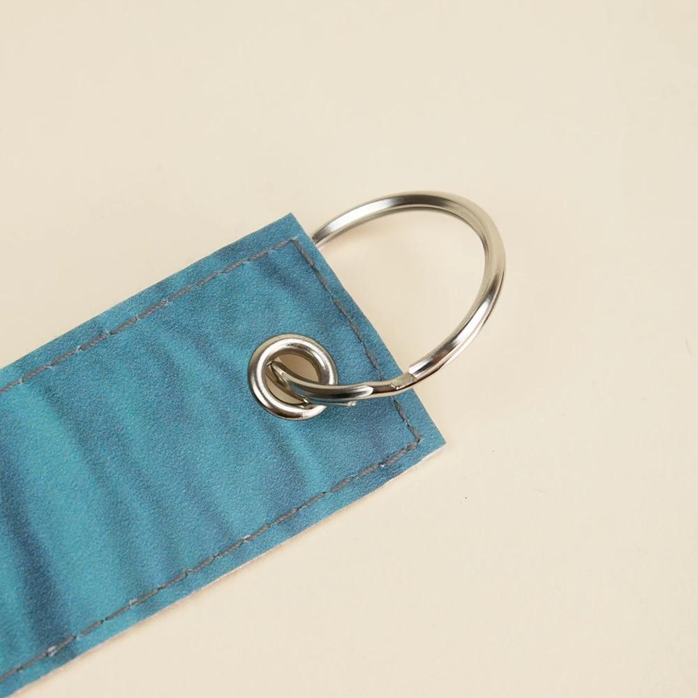 Llavero sostenible de lona LANIN Anilla y ojal metálicos de un llavero azul hecho con lona reciclada