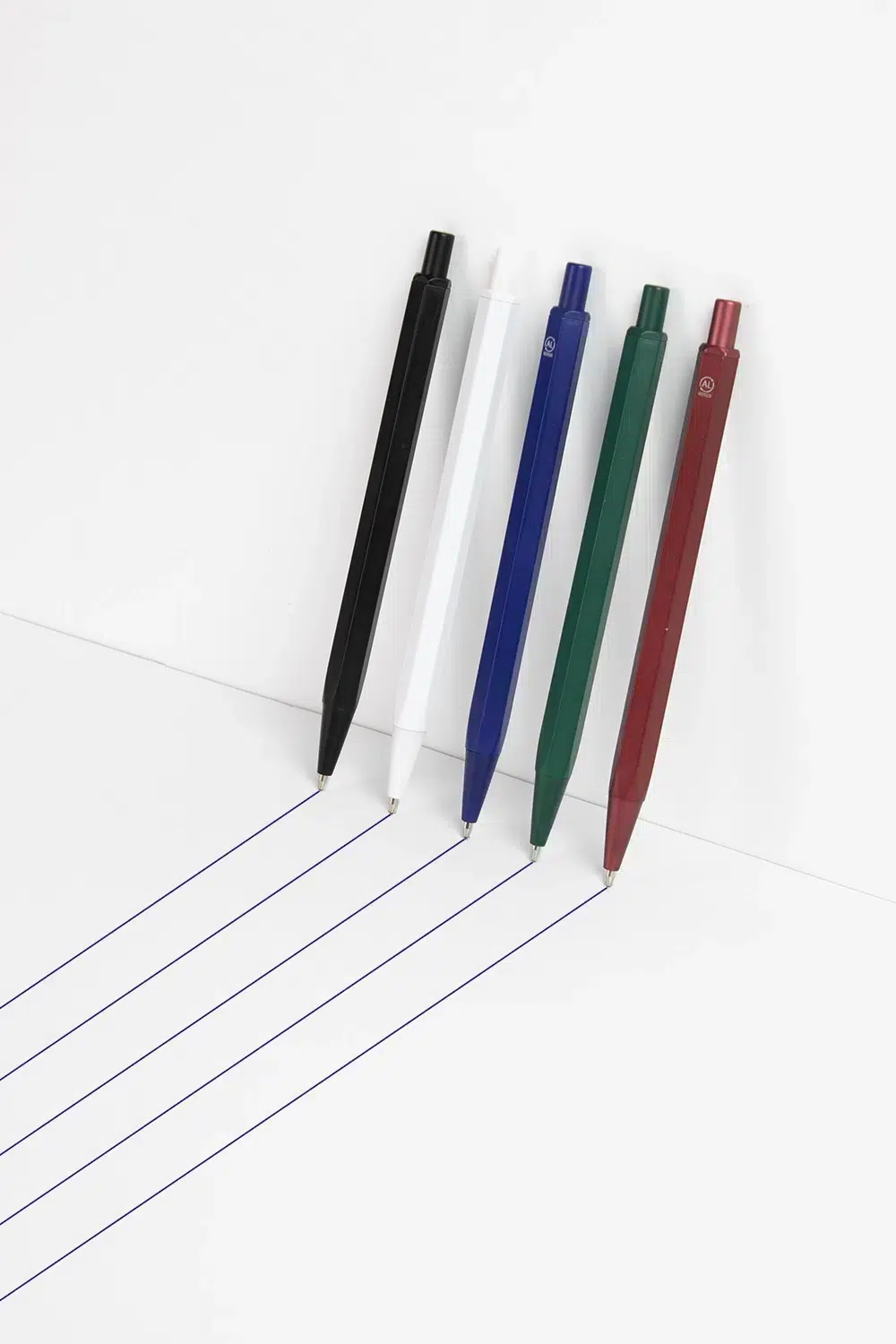 Cinco bolígrafos de aluminio trazando líneas sobre una superficie blanca