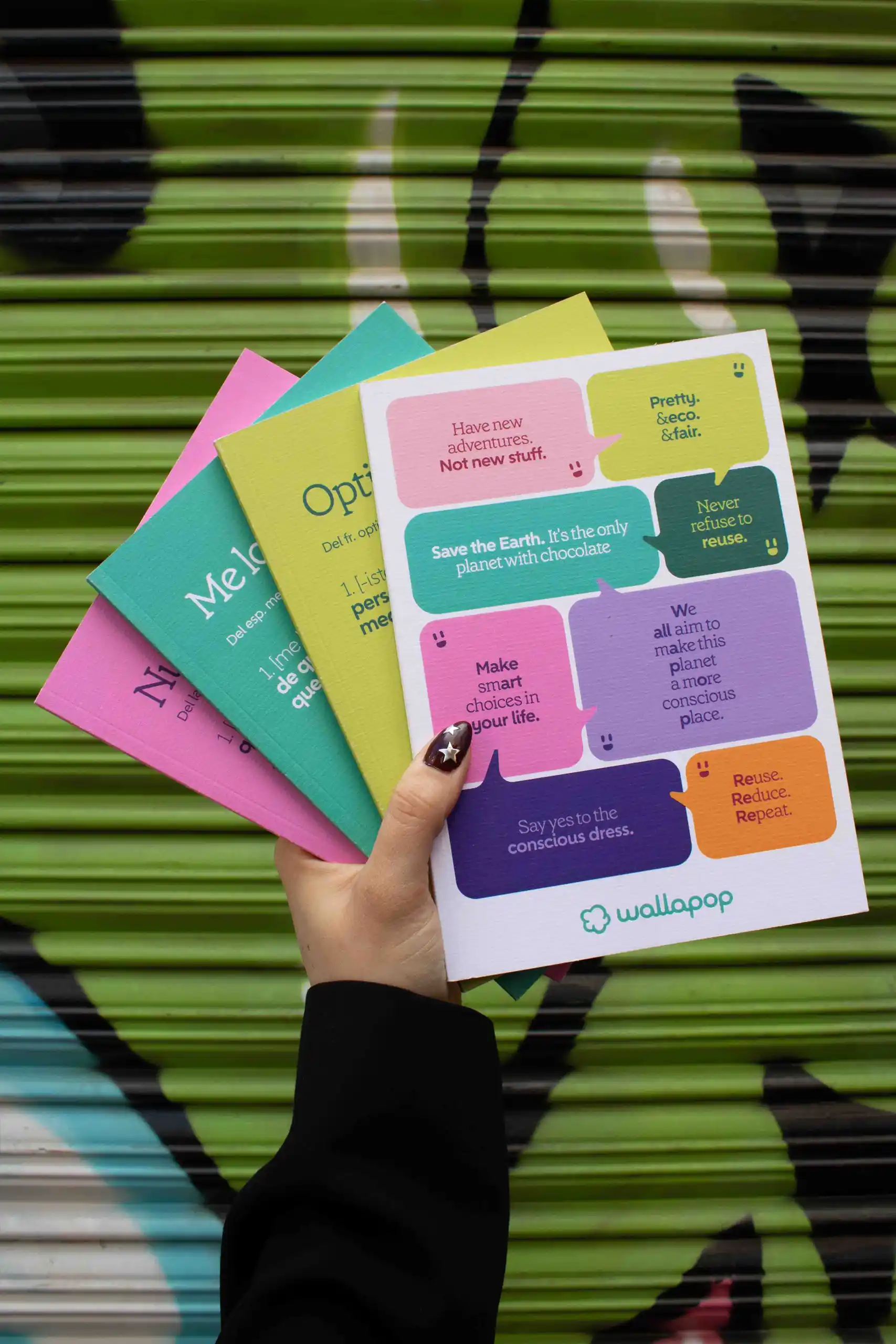 Mano mostrando varios cuadernos de colores personalizados para la marca WALLAPOP