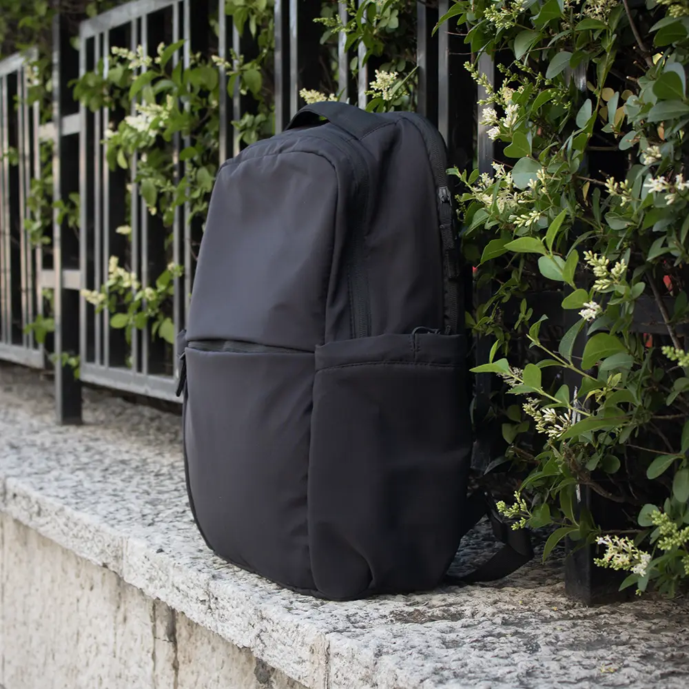 Personalised sustainable backpack for laptop FORMA Mochila urbana personalizada negra sobre bordillo con arbustos
