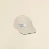 Gorra beige con logo lateral en un fondo beige