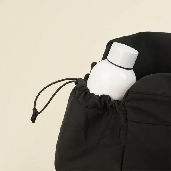 Botella blanca en uno de los bolsillos de una bolsa de deporte negra de poliéster reciclado