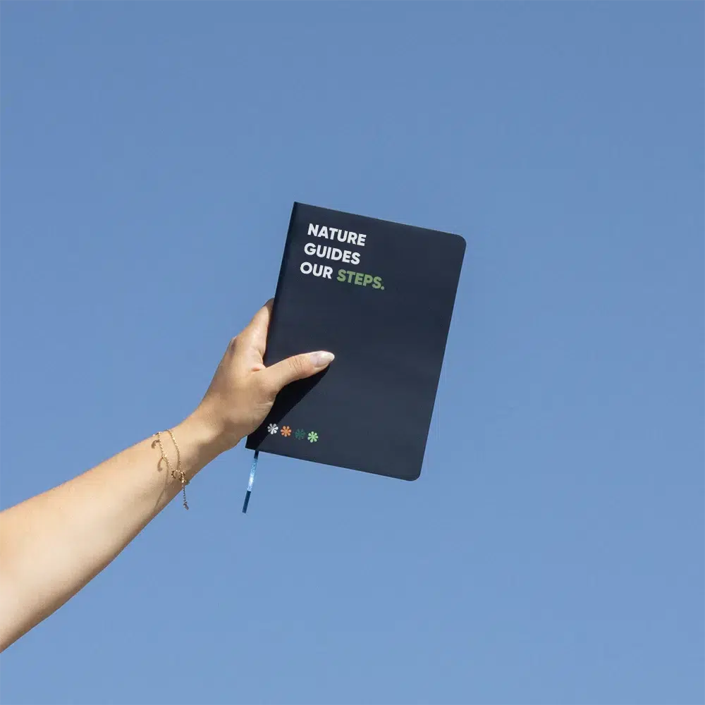 Mano alzando al cielo un cuaderno ecológico personalizado azul