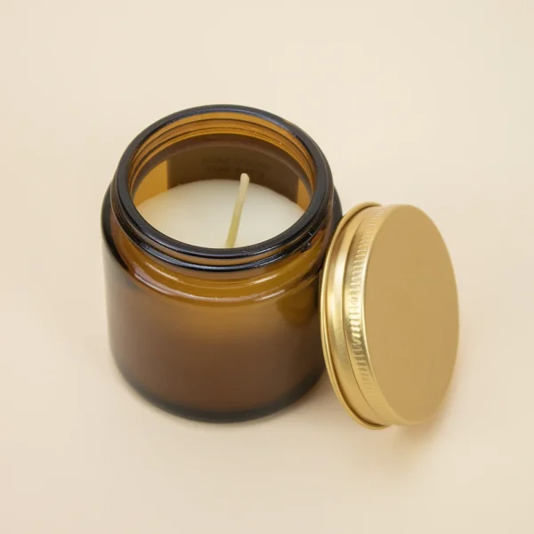 Vela aromática personalizada con tapa metálica sobre una superficie beige