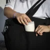 Manos guardando un vaso en una bolsa negra de viaje de algodón y poliéster reciclado
