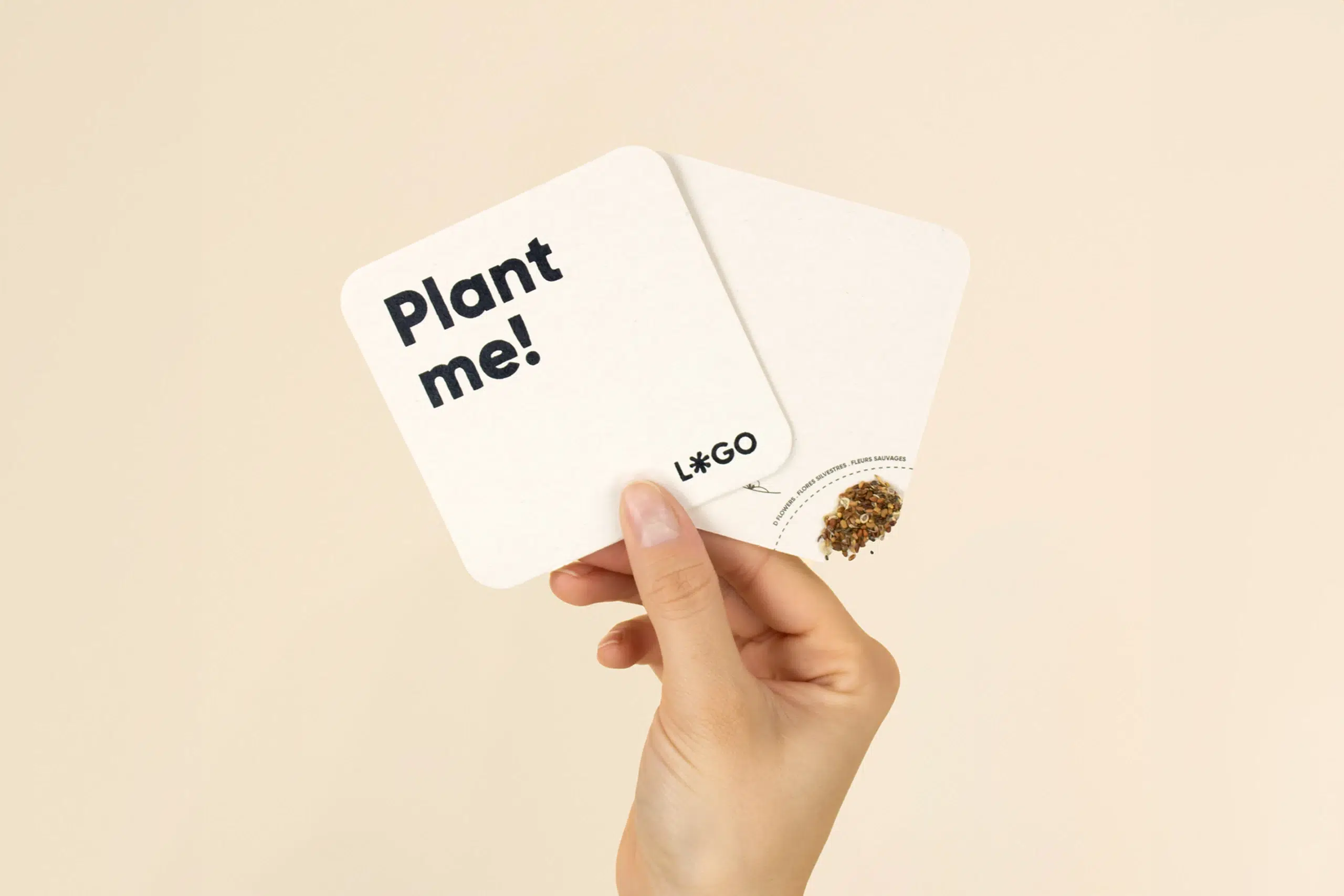 Una mano sujetando dos posavasos con semillas personalizados con la impresión de texto en azul 'Plant me"