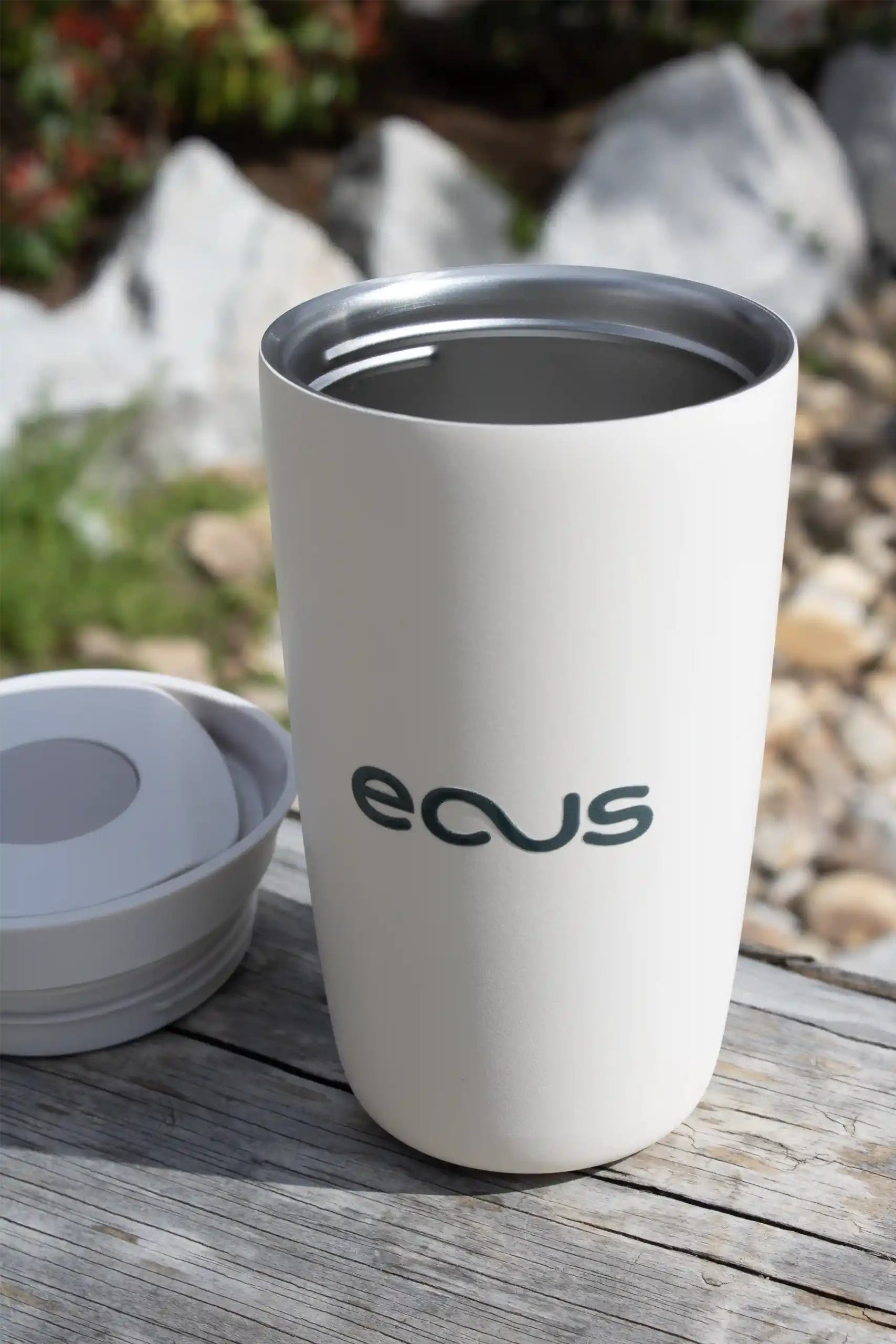 Termo abierto de color beige personalizado con el logo de la marca ECUS, apoyado en una piedra en el exterior