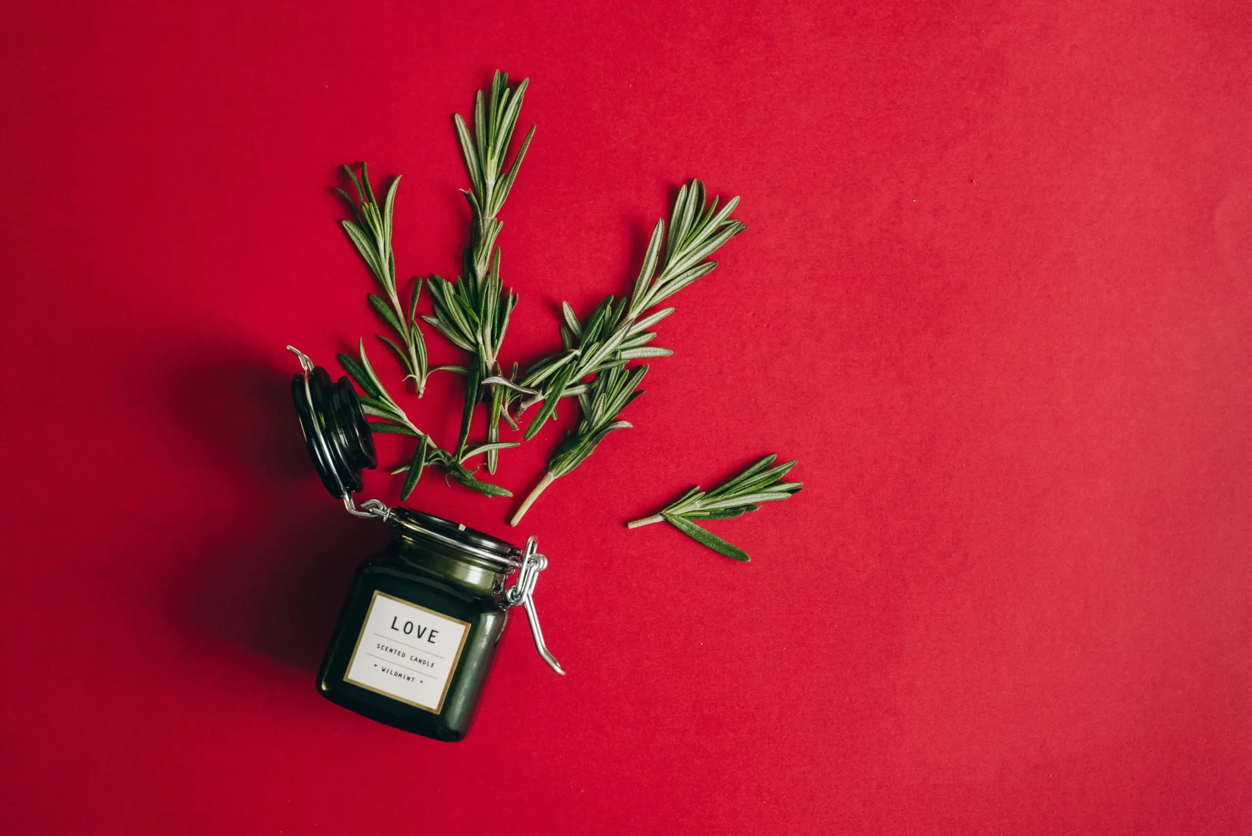 Regalos corporativos menos de 20 euros Vela personalizada junto a varias ramas de pino sobre una superficie de color rojo