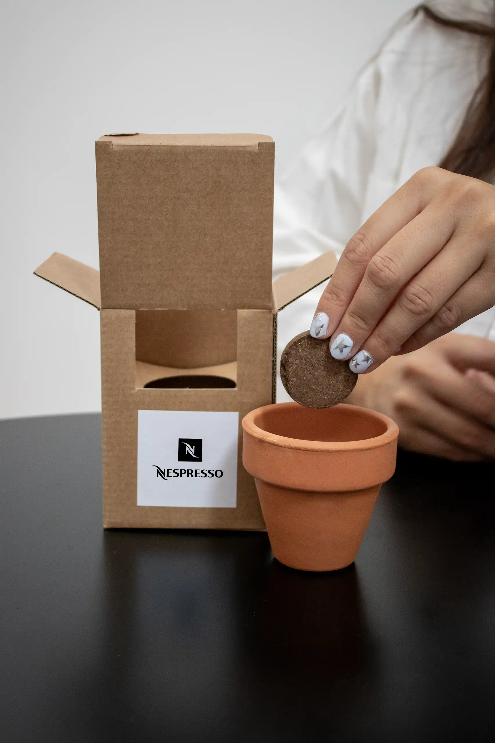 Mano colocando una pastilla de tierra dentro de un kit plantable de barro con una caja personalizada para la marca Nespresso