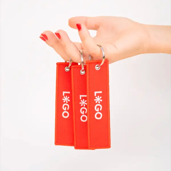 Llavero personalizado FILOS Mano sujetando 3 llaveros de tela rojos personalizados con logo blanco