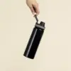 Botella deportiva personalizada BIBO Mano sosteniendo una botella deportiva negra personalizada en aluminio reciclado sobre un fondo beige