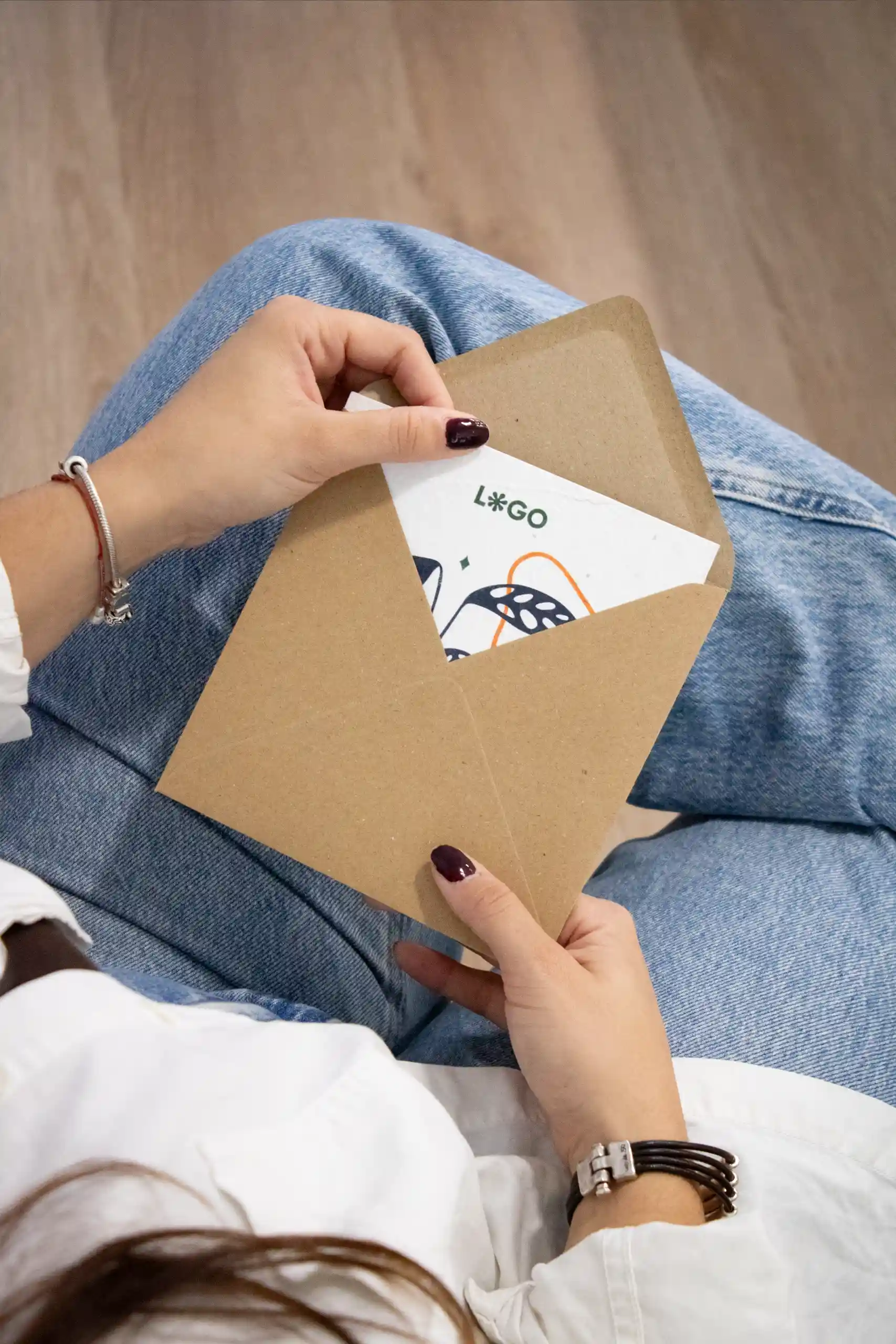 Imagen cenital de una chica sacando una tarjeta personalizada de un sobre kraft cuadrado
