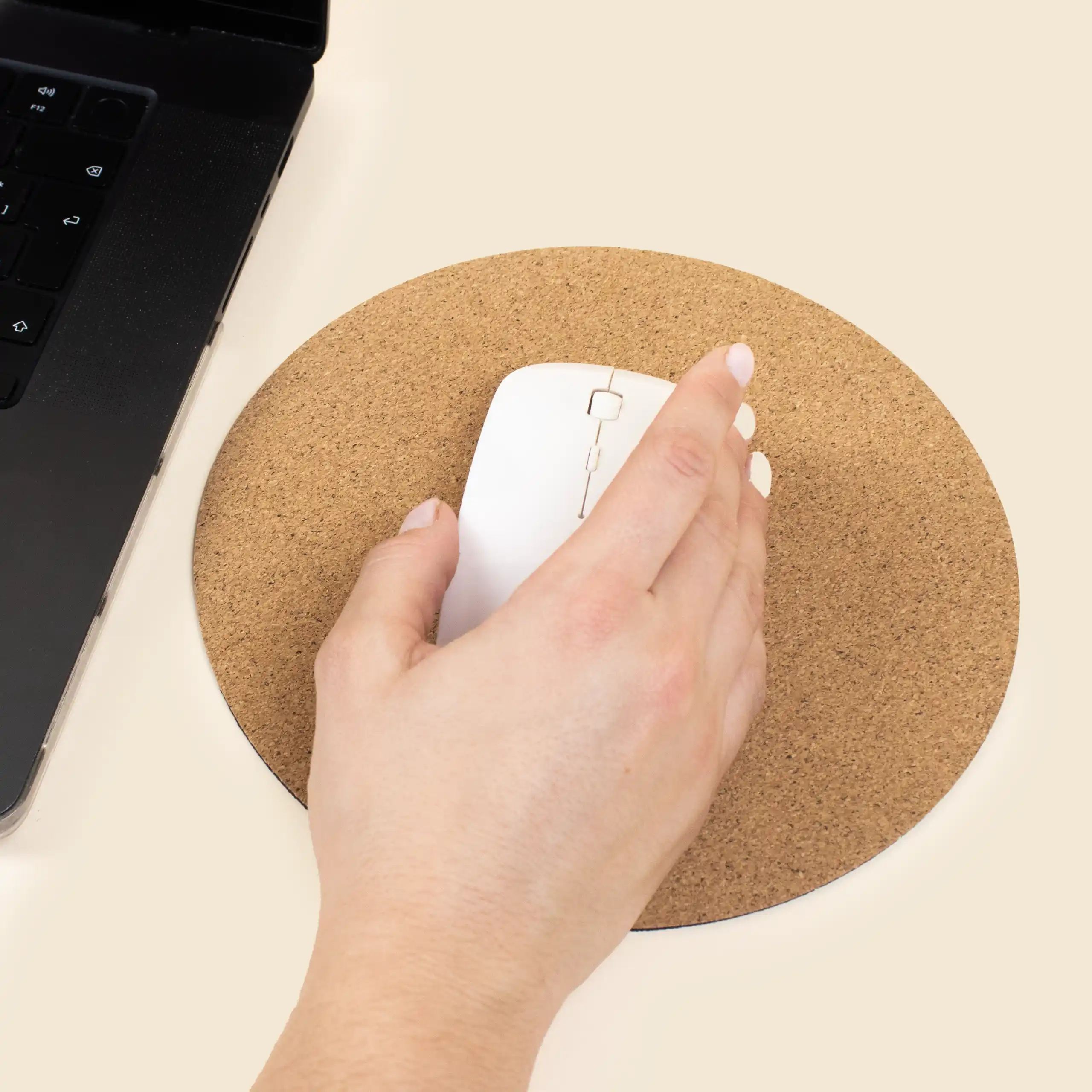 Alfombrilla de corcho personalizada CORA Mano sobre un ratón de ordenador blanco y una alfombrilla de corcho circular, junto a un ordenador portátil negro