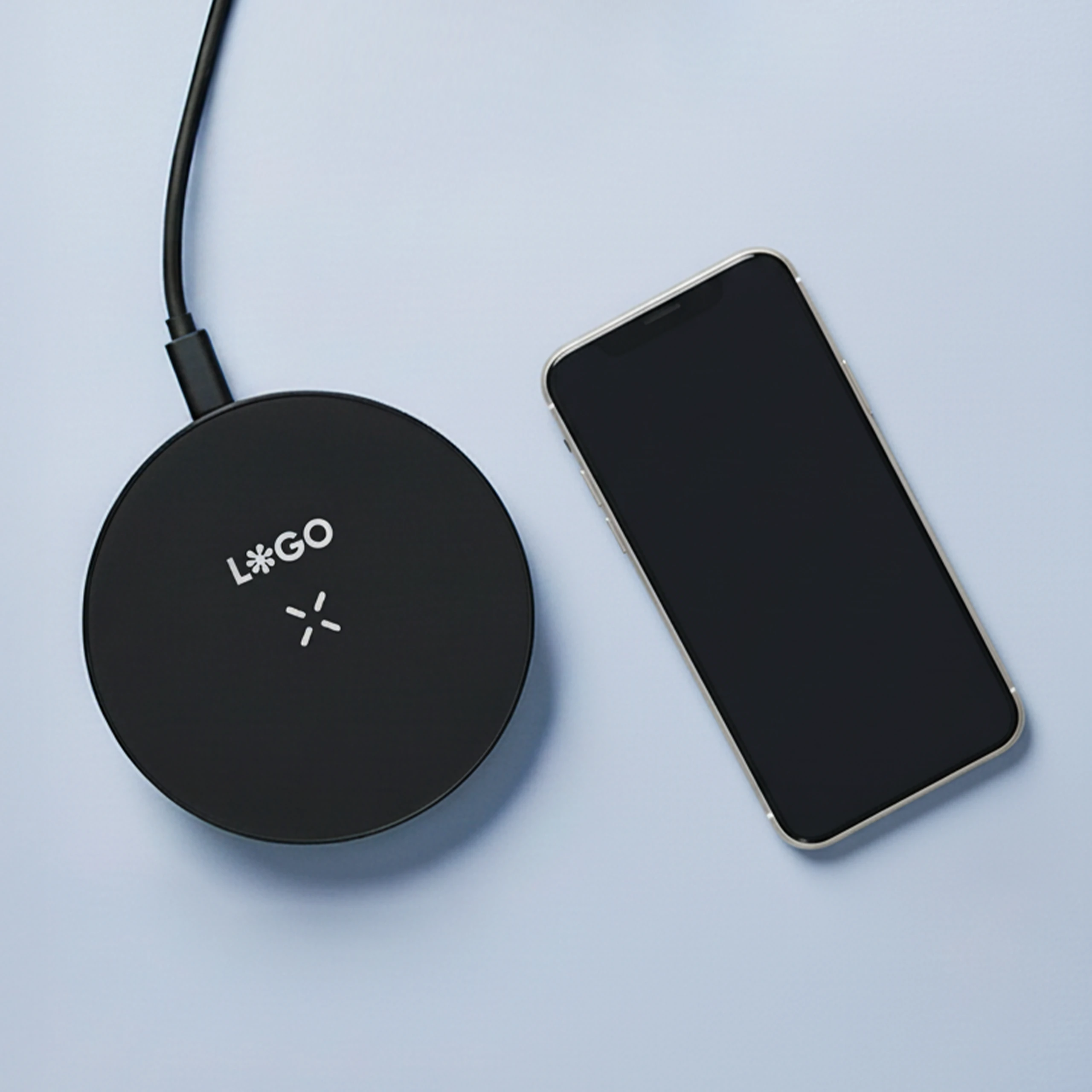 Cargador inalámbrico negro personalizado con la palabra 'LOGO' junto a un teléfono móvil iphone