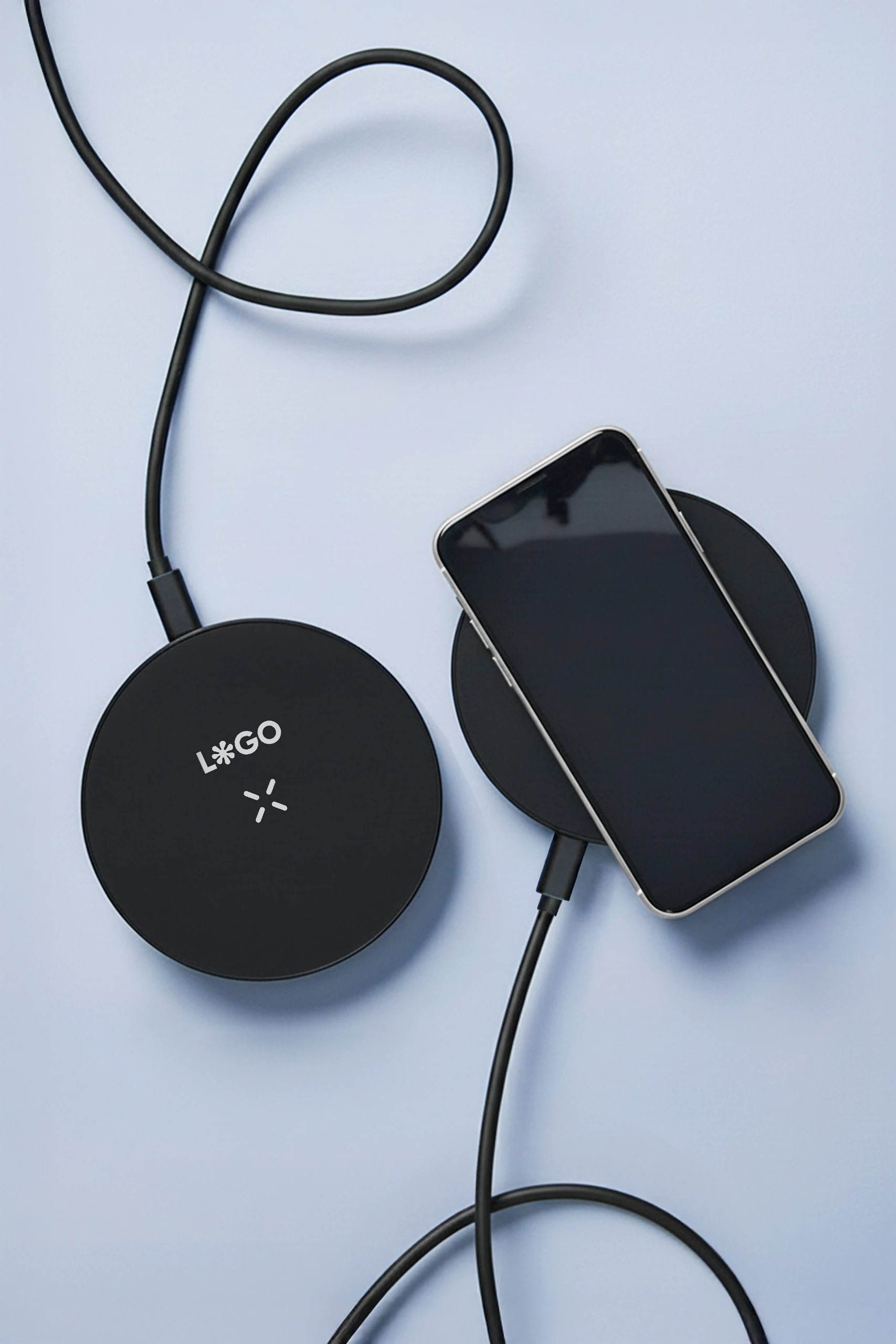 Dos cargadores inalámbricos negros personalizados con la palabra 'LOGO', junto a un teléfono móvil iphone