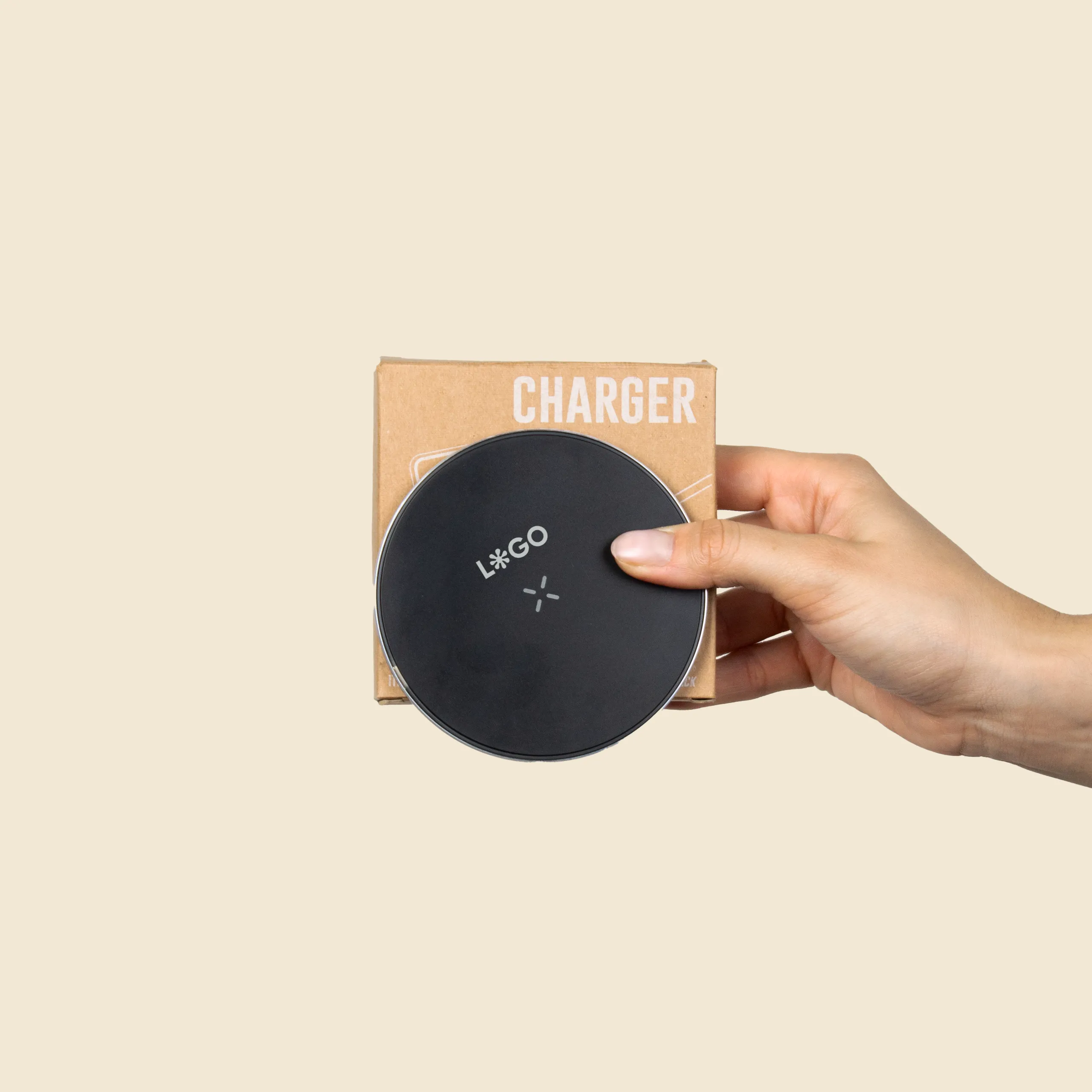 Mano sujetando un cargador inalámbrico negro personalizado con la palabra 'LOGO' junto a su caja de cartón