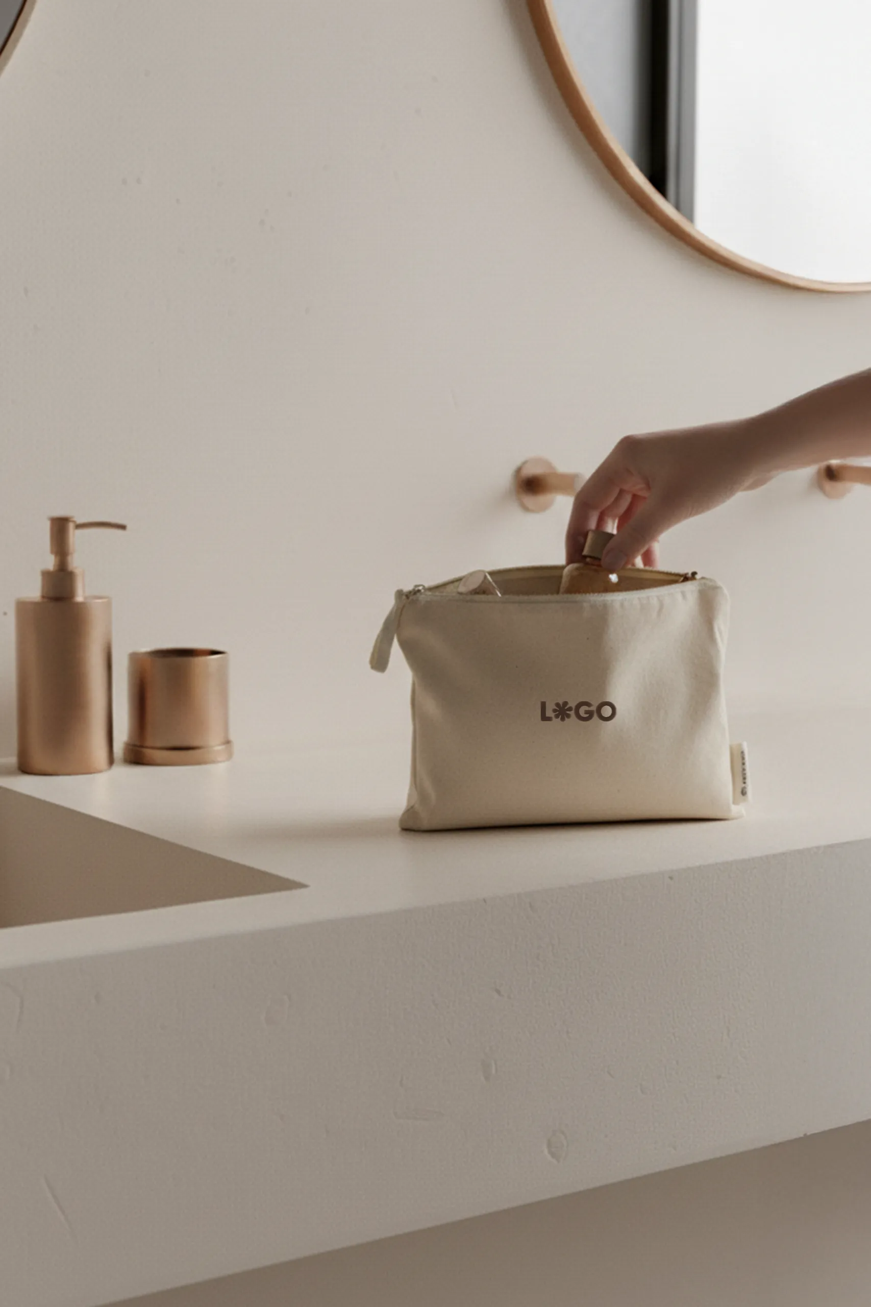 Mano metiendo un bote en un neceser beige de algodón personalizado con la palabra "LOGO" en marrón apoyado en la superficie de un lavabo de un baño