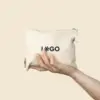 Mano sujetando un neceser beige de algodón personalizado con la palabra "LOGO" en negro