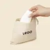 Mano metiendo un bote blanco en un neceser beige de algodón personalizado con la palabra "LOGO" en negro